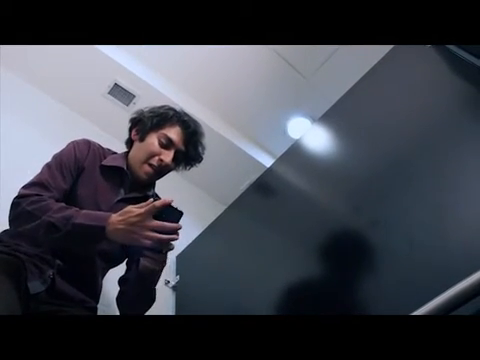 Fotograma original de ¿Y la foto?: contrapicado del personaje con su teléfono entre las divisiones del baño