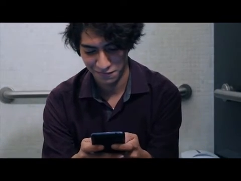 Fotograma original de ¿Y la foto?: plano medio del personaje sentado con su teléfono